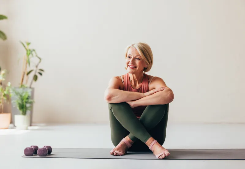 Smiling senior woman seated on a yoga mat at home